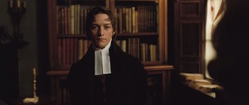 Movie still from “Becoming Jane” (2007), directed by Julian Jarrold – A man in a black coat and a white collar standing in front of a book shelf; Medium shot, Low angle
