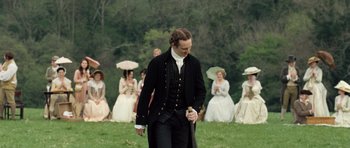 Movie still from “Becoming Jane” (2007), directed by Julian Jarrold – A man in a black coat and black pants walking in front of a group of people; Medium shot, Over the shoulder angle