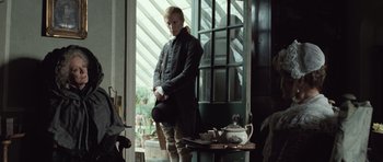 Movie still from “Becoming Jane” (2007), directed by Julian Jarrold – A man in a black coat standing in front of a window; Medium shot, Low angle