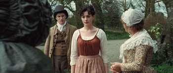 Movie still from “Becoming Jane” (2007), directed by Julian Jarrold – A woman in a brown dress standing in front of two men; Medium shot, Over the shoulder angle