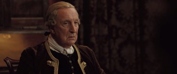 Movie still from “Becoming Jane” (2007), directed by Julian Jarrold – An older man in a brown and gold jacket; Close Up shot, Over the shoulder angle