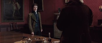 Movie still from “Becoming Jane” (2007), directed by Julian Jarrold – A man standing in front of a dining room table; Medium shot, Over the shoulder angle