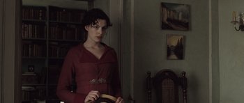 Movie still from “Becoming Jane” (2007), directed by Julian Jarrold – A woman in a red dress holding an object in a room; Medium shot, Over the shoulder angle