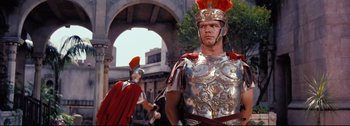 Movie still from “Ben-Hur” (1959), directed by William Wyler – A man in a helmet and armor stands next to another man in a helmet and armor; Medium shot, Low angle
