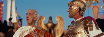Movie still from “Ben-Hur” (1959), directed by William Wyler – Two men are standing next to each other in front of an angel statue; Medium shot, Low angle