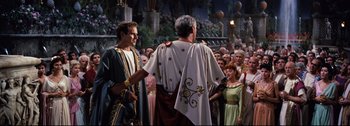 Movie still from “Ben-Hur” (1959), directed by William Wyler – A group of people standing in front of a crowd wearing costumes; Medium shot, Over the shoulder angle