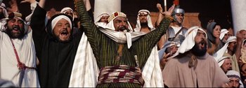 Movie still from “Ben-Hur” (1959), directed by William Wyler – A man with a beard is wearing a turban and holding his hands up; Medium shot, Low angle