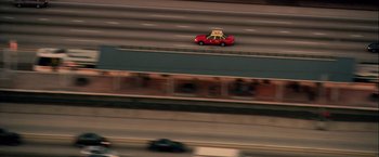 Movie still from “Collateral” (2004), directed by Michael Mann – A red car driving down a street next to a bridge; Extreme Wide shot, High angle