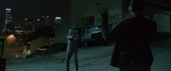 Movie still from “Collateral” (2004), directed by Michael Mann – Two men in a parking lot , one holding a gun and the other holding his hand up to his face; Wide shot, Over the shoulder angle