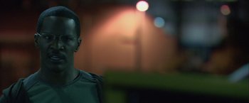 Movie still from “Collateral” (2004), directed by Michael Mann – A man in a green shirt is standing in front of some lights; Close Up shot, Over the shoulder angle