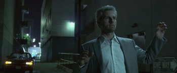 Movie still from “Collateral” (2004), directed by Michael Mann – A man in a white shirt and a jacket is holding a cigarette; Medium shot, Low angle