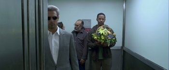 Movie still from “Collateral” (2004), directed by Michael Mann – A group of men standing next to each other holding flowers; Medium shot, Over the shoulder angle