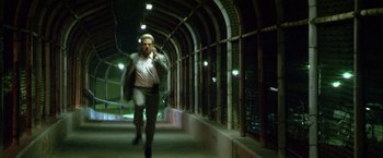 Movie still from “Collateral” (2004), directed by Michael Mann – A man walking down a hallway at night talking on a phone; Wide shot, Low angle