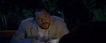 Movie still from “Collateral” (2004), directed by Michael Mann – A man sitting at a table with a drink in front of him; Close Up shot, Over the shoulder angle