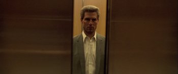 Movie still from “Collateral” (2004), directed by Michael Mann – A man in a gray suit and white shirt in an elevator; Medium shot, Low angle