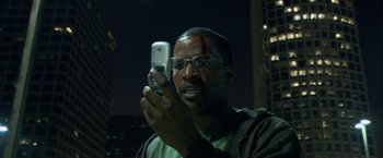 Movie still from “Collateral” (2004), directed by Michael Mann – A man holding up a cell phone in front of him; Close Up shot, Low angle
