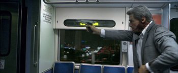 Movie still from “Collateral” (2004), directed by Michael Mann – A man holding a gun in front of a train window; Medium shot, Low angle