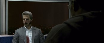 Movie still from “Collateral” (2004), directed by Michael Mann – A man wearing a suit and tie sitting in front of a window; Close Up shot, Over the shoulder angle