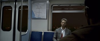 Movie still from “Collateral” (2004), directed by Michael Mann – A man in a suit sitting on a train; Medium shot, Over the shoulder angle