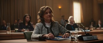 Movie still from “Black Panther: Wakanda Forever” (2022), directed by Ryan Coogler – A woman sitting at a table with papers in front of a microphone; Medium shot, Over the shoulder angle