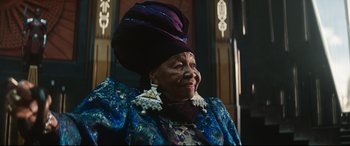 Movie still from “Black Panther: Wakanda Forever” (2022), directed by Ryan Coogler – An older woman wearing a purple hat and a blue dress; Medium shot, Low angle