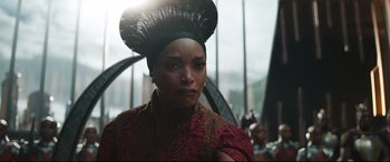 Movie still from “Black Panther: Wakanda Forever” (2022), directed by Ryan Coogler – A woman in a red and black dress with a hat on her head; Close Up shot, Over the shoulder angle