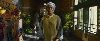 Movie still from “Black Panther: Wakanda Forever” (2022), directed by Ryan Coogler – A woman wearing a turban standing in front of a building; Medium shot, Low angle