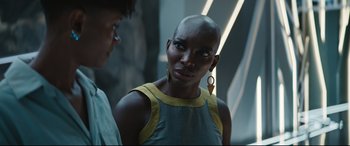Movie still from “Black Panther: Wakanda Forever” (2022), directed by Ryan Coogler – A woman in a yellow and blue dress with a earring; Close Up shot, Over the shoulder angle