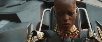 Movie still from “Black Panther: Wakanda Forever” (2022), directed by Ryan Coogler – A woman with a bald head wearing gold jewelry; Close Up shot, Over the shoulder angle
