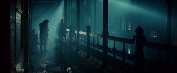 Movie still from “Blade Runner” (1982), directed by Ridley Scott – A person standing in a dark room next to a railing; Wide shot, Low angle
