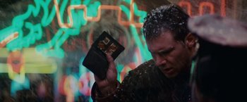 Movie still from “Blade Runner” (1982), directed by Ridley Scott – A man is holding a wallet in front of a colorful background; Close Up shot, Low angle