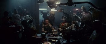 Movie still from “Blade Runner” (1982), directed by Ridley Scott – A group of people sitting at a table in a dark room; Wide shot, High angle
