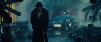 Movie still from “Blade Runner” (1982), directed by Ridley Scott – A man in a hat and coat standing in front of a cop car; Medium shot, Over the shoulder angle
