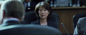 Movie still from “Blood Diamond” (2006), directed by Edward Zwick – A woman sitting in a chair in an office setting; Close Up shot, Over the shoulder angle