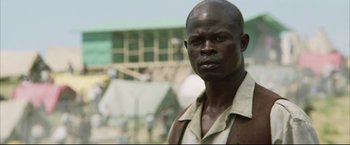 Movie still from “Blood Diamond” (2006), directed by Edward Zwick – A man in a brown and white shirt is looking at the camera; Close Up shot, Low angle