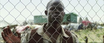 Movie still from “Blood Diamond” (2006), directed by Edward Zwick – A man standing in front of a chain link fence; Close Up shot, Low angle