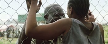 Movie still from “Blood Diamond” (2006), directed by Edward Zwick – A woman standing next to a man behind a chain link fence; Close Up shot, Over the shoulder angle