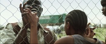 Movie still from “Blood Diamond” (2006), directed by Edward Zwick – A man and a woman standing next to each other in front of a chain link fence; Medium shot, Low angle