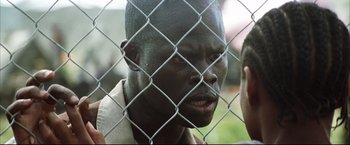 Movie still from “Blood Diamond” (2006), directed by Edward Zwick – A person behind a chain link fence; Close Up shot, Over the shoulder angle
