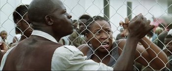 Movie still from “Blood Diamond” (2006), directed by Edward Zwick – A group of people behind a chain link fence; Close Up shot, Low angle