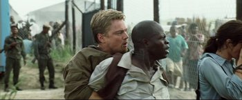 Movie still from “Blood Diamond” (2006), directed by Edward Zwick – A man is carrying another man on his back; Medium shot, Over the shoulder angle