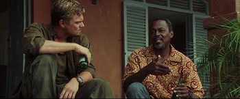 Movie still from “Blood Diamond” (2006), directed by Edward Zwick – Two men sitting on the ground talking to each other; Medium shot, Over the shoulder angle
