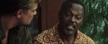 Movie still from “Blood Diamond” (2006), directed by Edward Zwick – A man talking to another man in front of a wall; Close Up shot, Over the shoulder angle