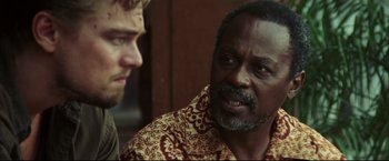 Movie still from “Blood Diamond” (2006), directed by Edward Zwick – Two men are talking to each other in front of a wooden wall; Close Up shot, Over the shoulder angle