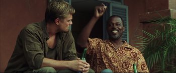 Movie still from “Blood Diamond” (2006), directed by Edward Zwick – Two men sitting next to each other holding a bottle; Medium shot, Low angle