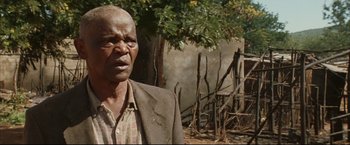 Movie still from “Blood Diamond” (2006), directed by Edward Zwick – An older man standing in front of a tree; Close Up shot, Over the shoulder angle