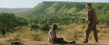 Movie still from “Blood Diamond” (2006), directed by Edward Zwick – A man sitting on the ground in the grass; Extreme Wide shot, Low angle