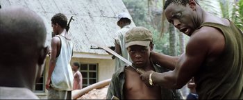 Movie still from “Blood Diamond” (2006), directed by Edward Zwick – A young man is holding a knife in his hand; Medium shot, Over the shoulder angle