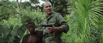 Movie still from “Blood Diamond” (2006), directed by Edward Zwick – A man holding a gun in his hand while standing next to a young boy; Medium shot, Over the shoulder angle