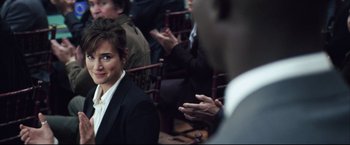 Movie still from “Blood Diamond” (2006), directed by Edward Zwick – A woman in a black suit is sitting in front of other people; Close Up shot, Over the shoulder angle